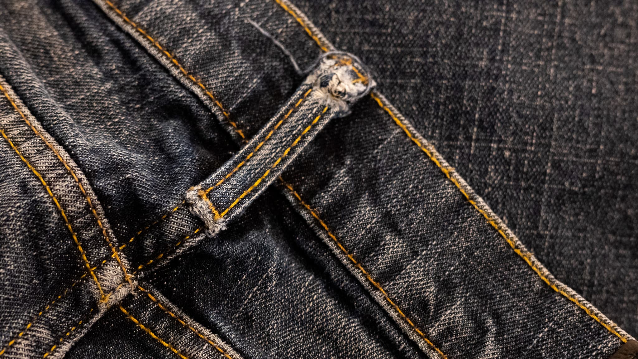 Close-up of a frayed belt loop on a pair of dark denim jeans.