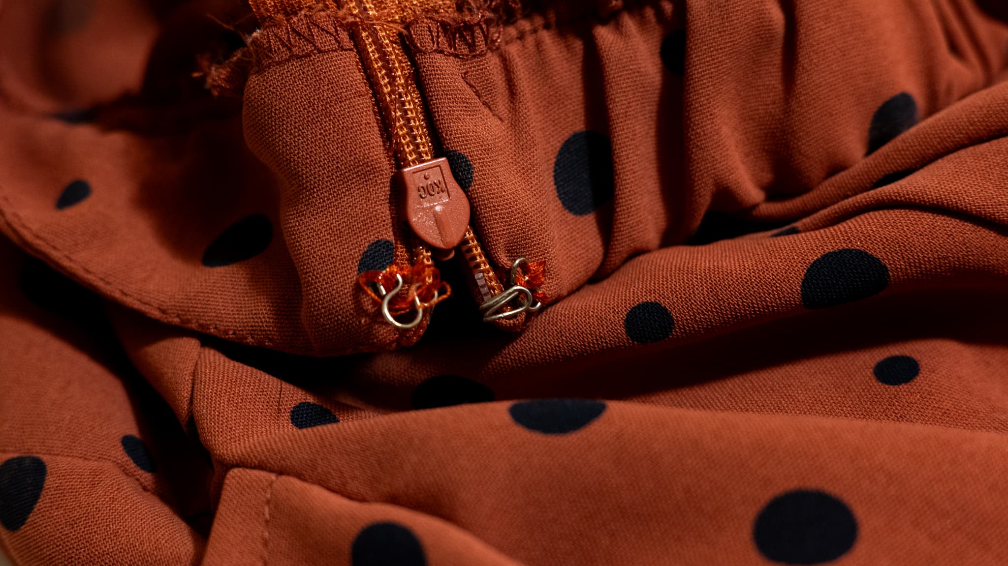 Close-up of a zipper and hook-and-eye closure on a rust polka-dot dress.